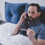 Kranker Mann im Bett mit Fieberthermometer und Telefon