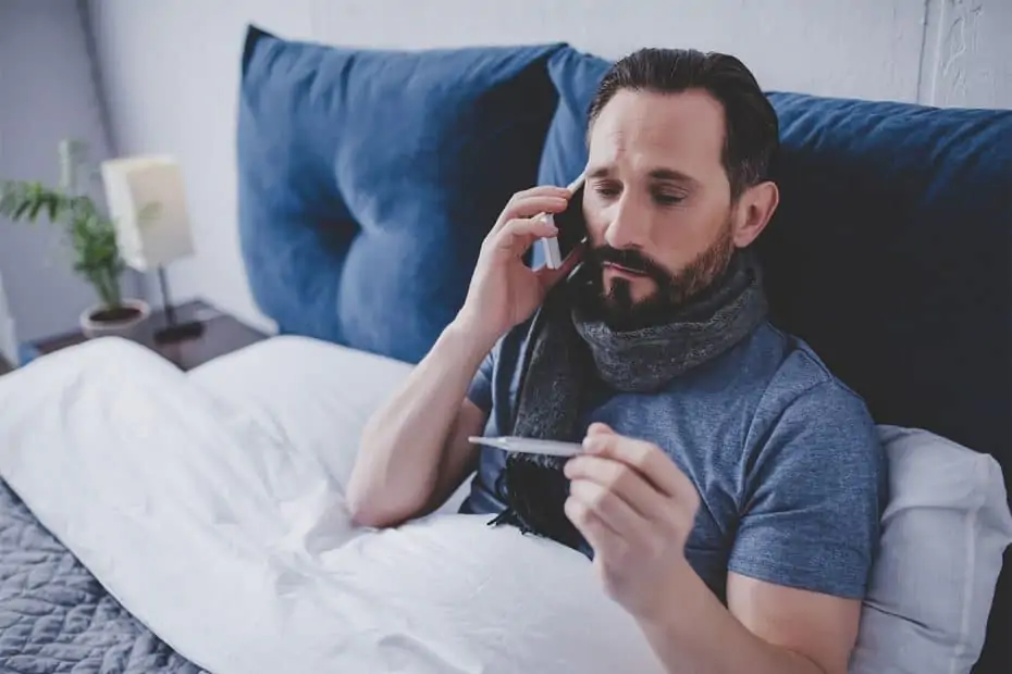 Kranker Mann im Bett mit Fieberthermometer und Telefon